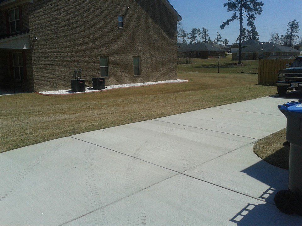 Concrete driveway next to a brick building and patchy grass lawn on a sunny day.
