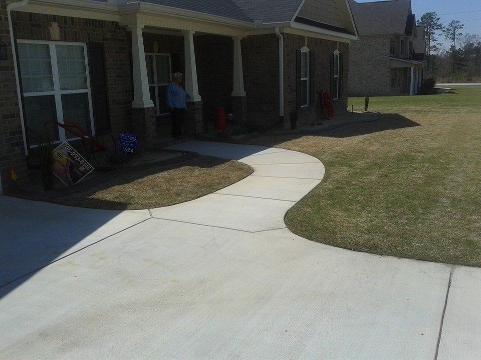 Concrete walkway curves from driveway to porch of a brick house.