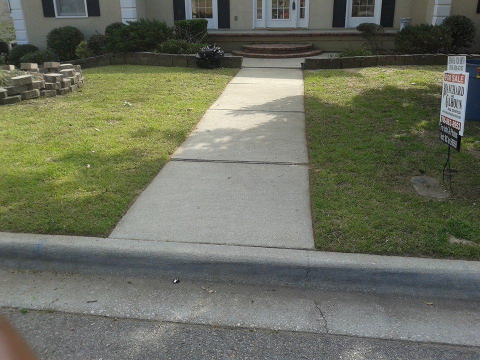 Concrete walkway leading to a house with a lawn, grass, and a for sale sign.