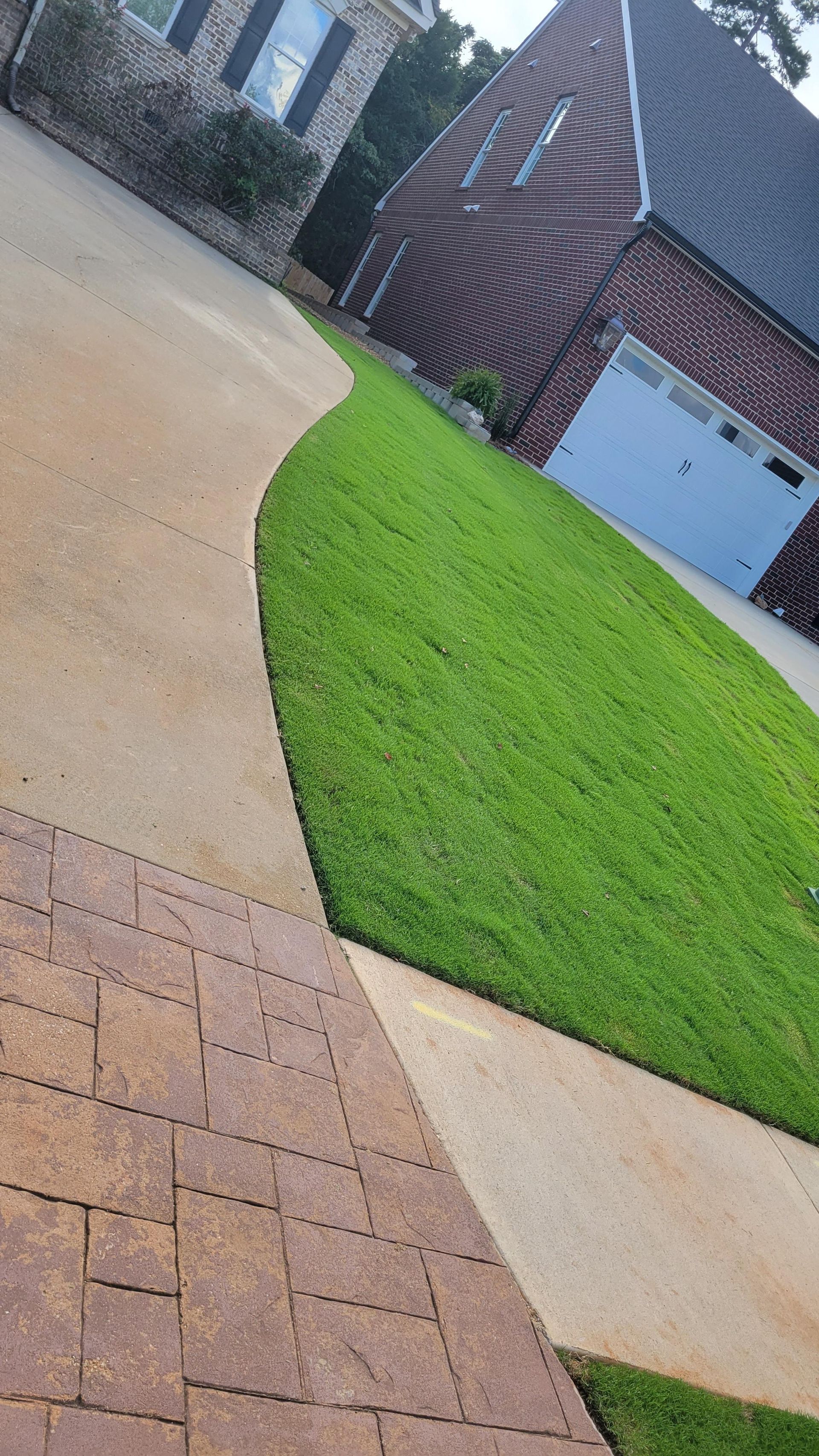 Driveway and green lawn leading to a brick house with a white garage door.