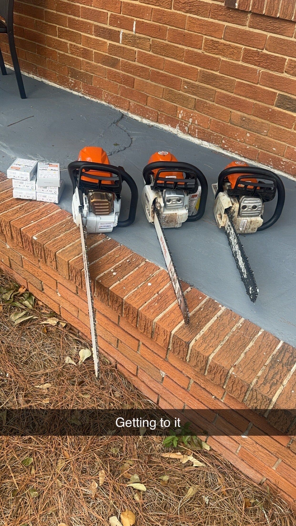 Three chainsaws on a brick ledge. The chainsaws are gray, orange, and black. 