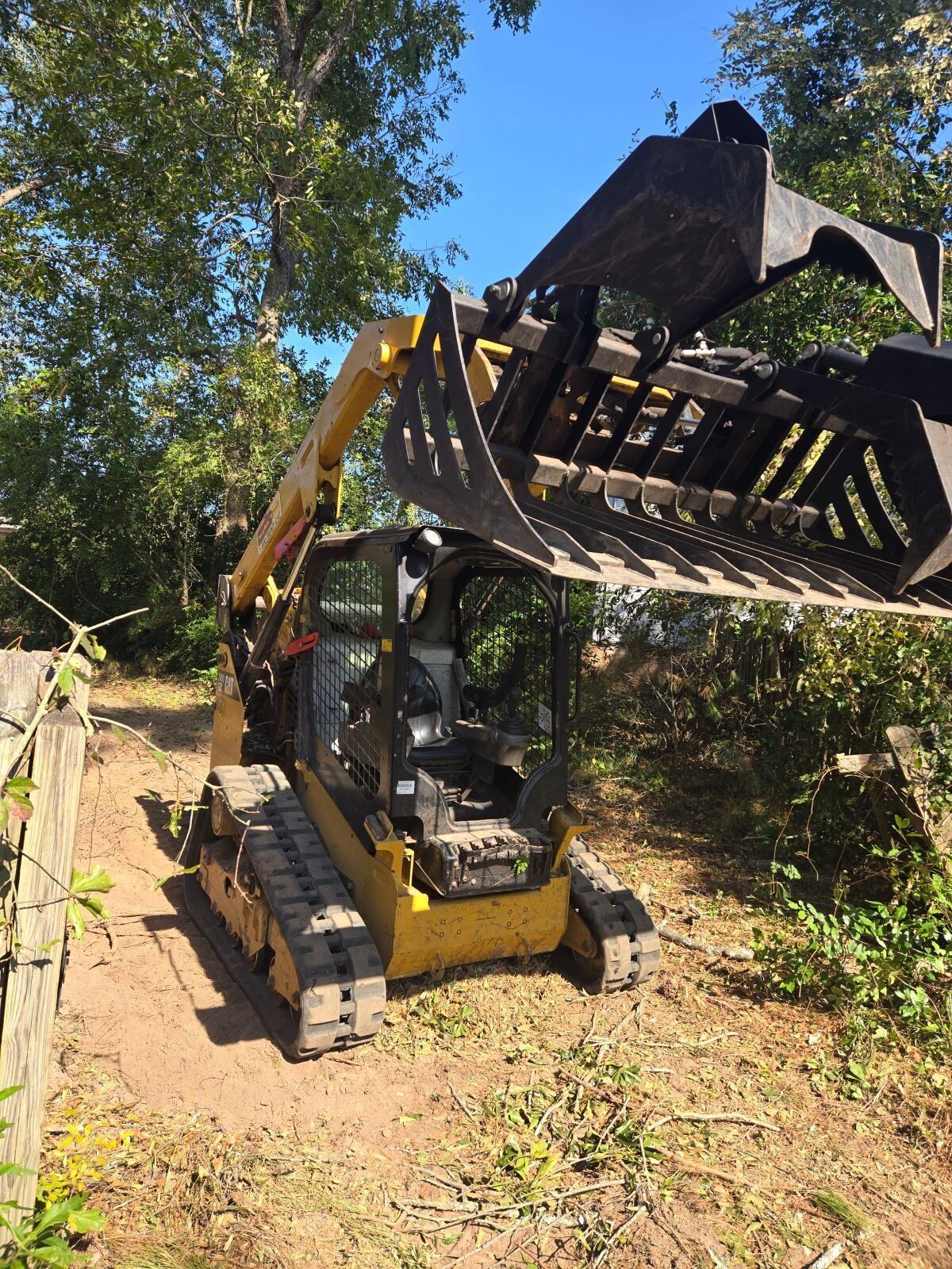 Yellow skid steer with grapple attachment in a wooded area.