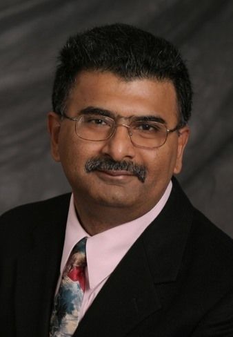 Man in suit, glasses, and a mustache, smiling, professional portrait.