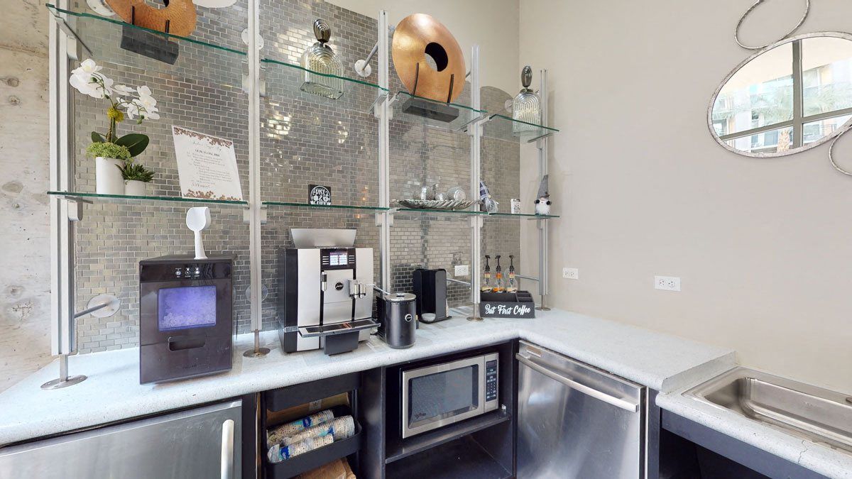 A modern coffee station here at Skyline Lofts Apartments with a silver coffee machine, syrup bottles, and a sign reading 