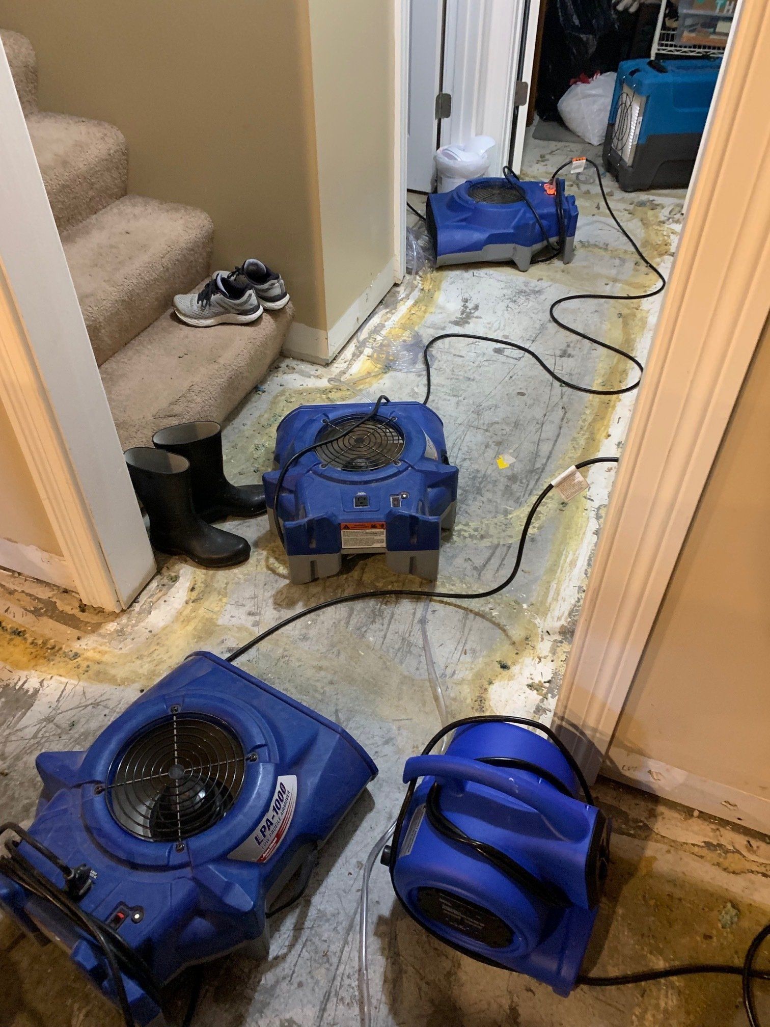 Blue air movers in a room with water damage near stairs.