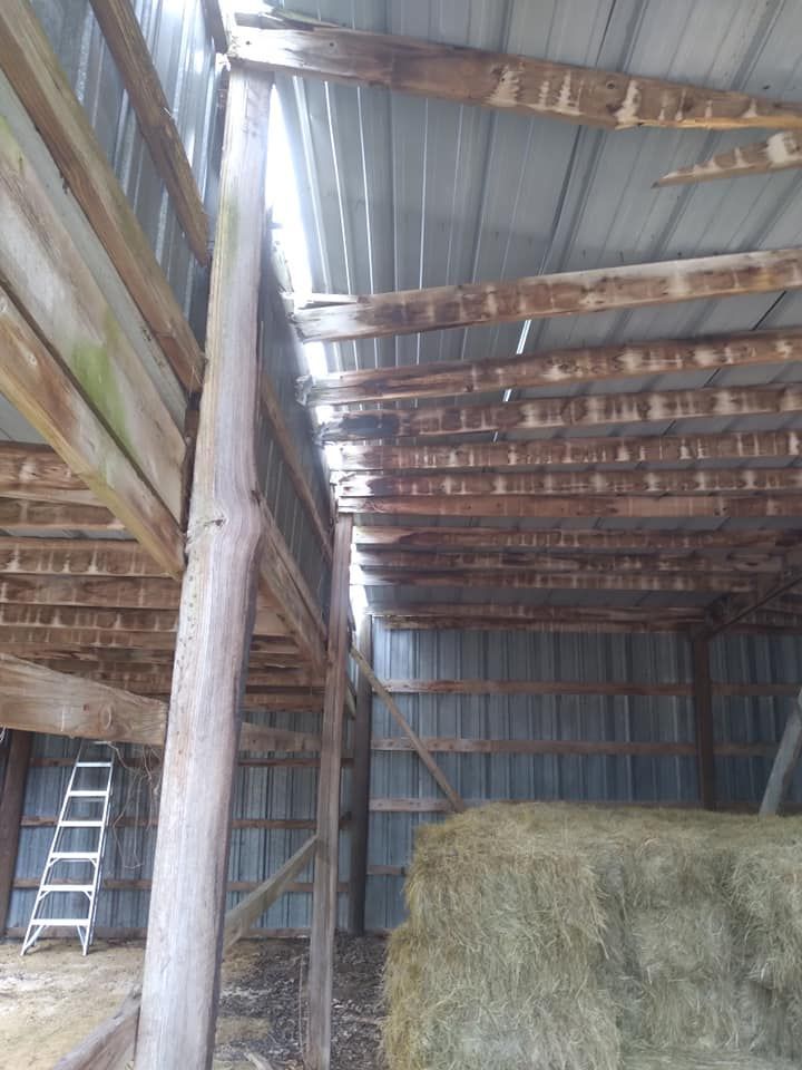 Inside of a dilapidated barn with visible wood beams and a metal roof. A stack of hay is on the right.
