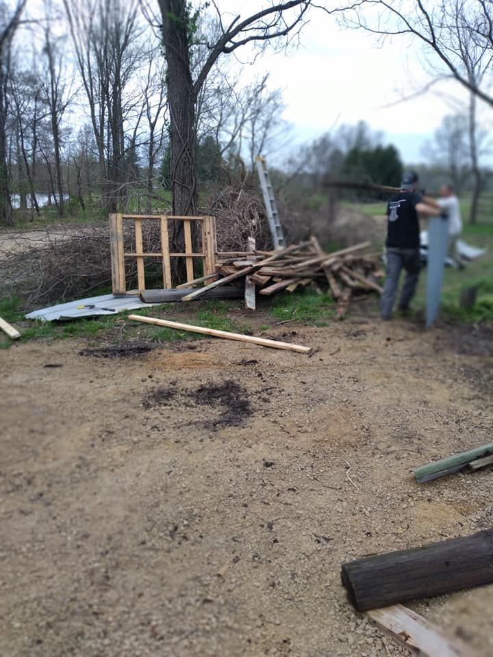 Outdoor scene with wood scraps, a pallet, and two people near a fence.