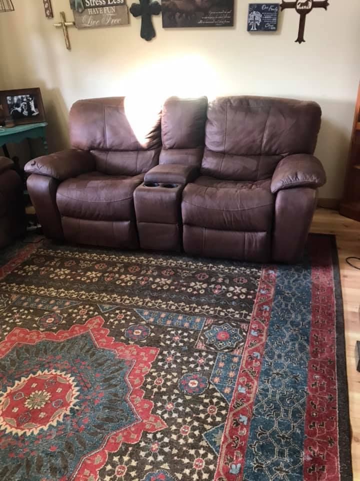 Brown reclining loveseat with cupholders on a patterned rug.