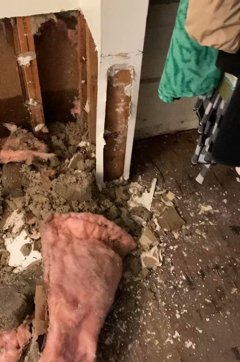Damaged interior corner with exposed wood, insulation, and debris.