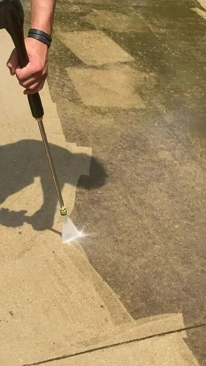 Person power washing a concrete surface, cleaning a dirty section with a spray nozzle.