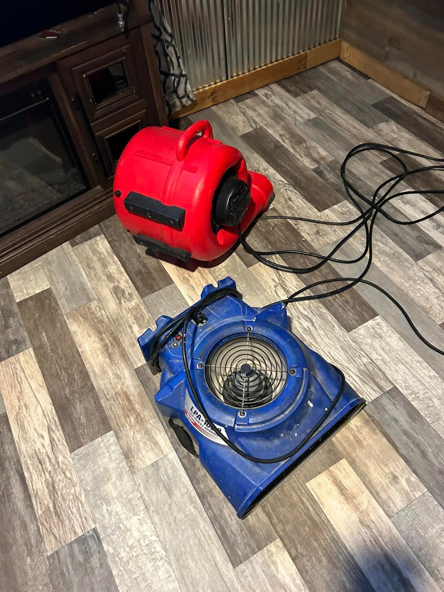 Red and blue air movers on wood-look floor near a fireplace.
