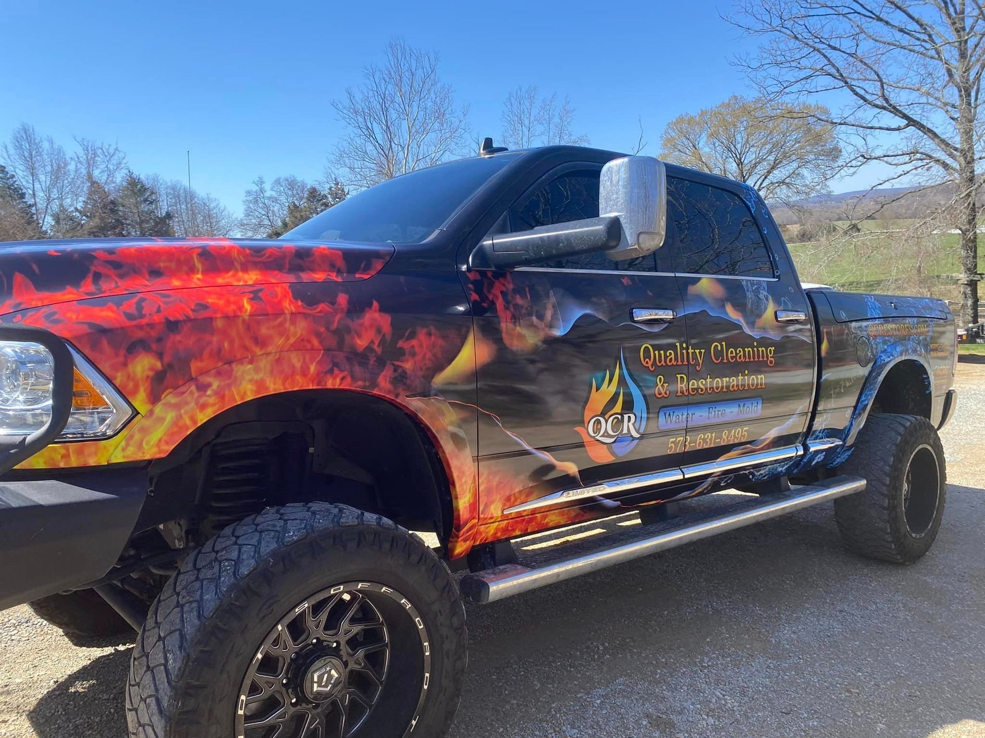 Black pickup truck with flame design wrap and business logo parked outdoors.