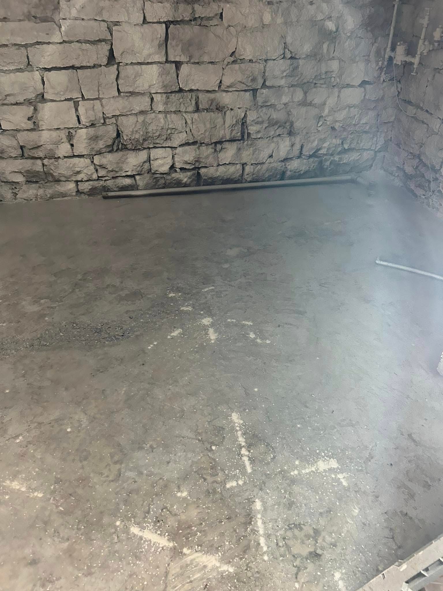 Concrete floor in a basement, gray brick wall, and a gray pipe.