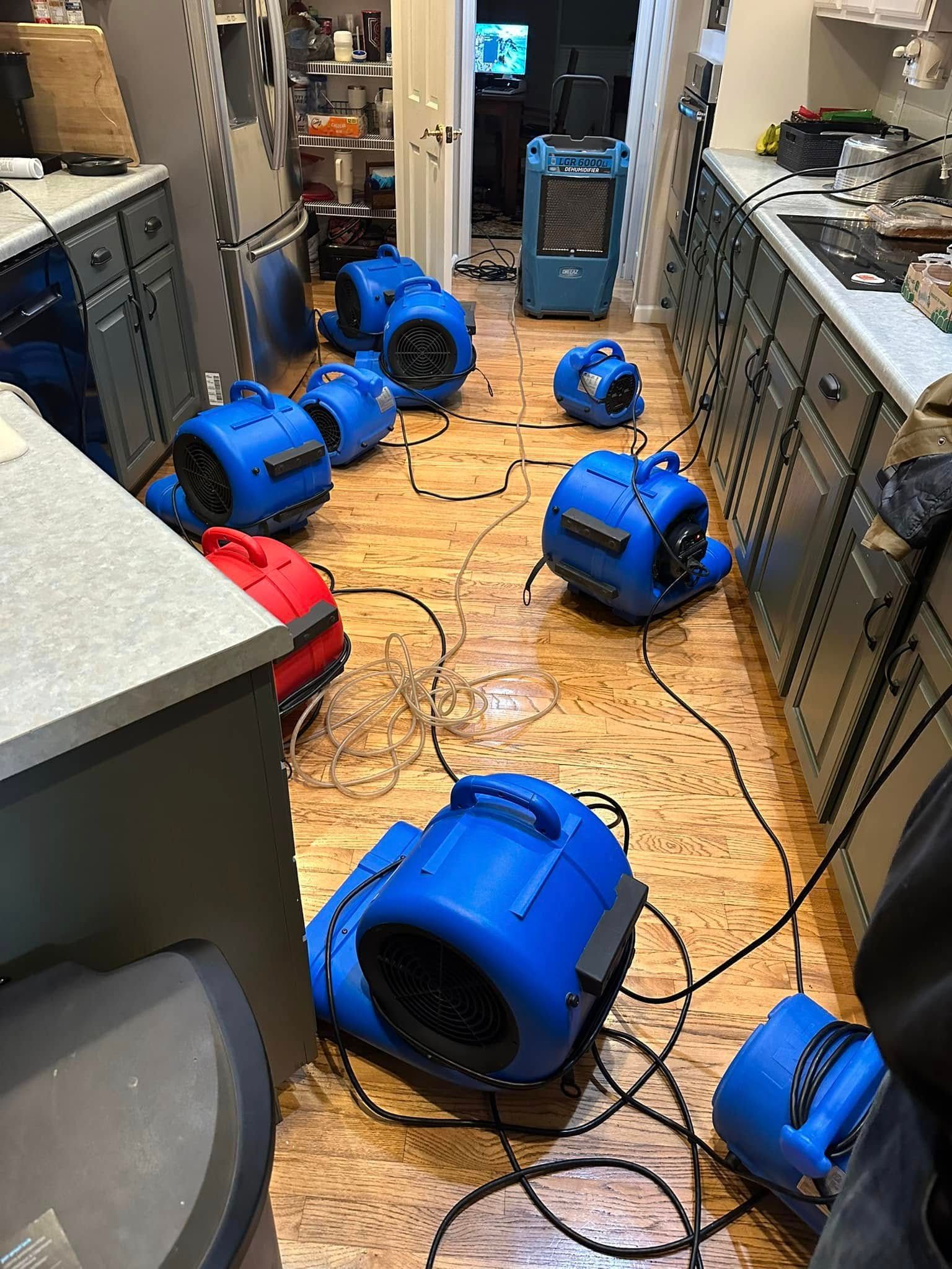 Blue air movers drying a kitchen floor after a water leak.