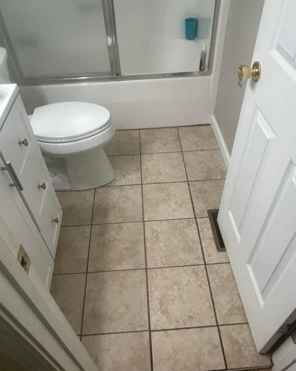 Bathroom with beige tile floor, toilet, vanity, and shower/tub. A white door is on the right.