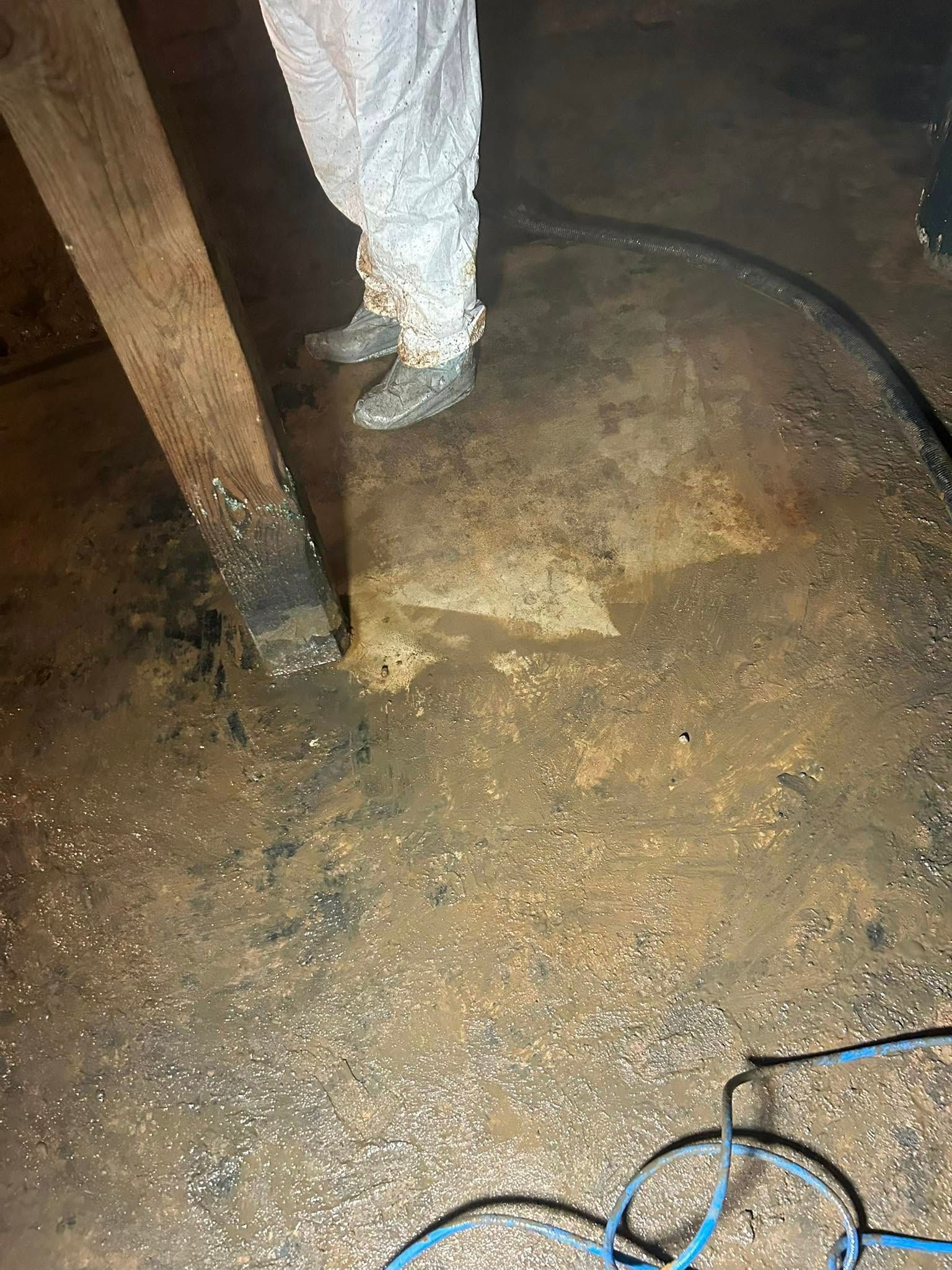 Person in protective suit standing on wet, dark floor next to wooden beam.