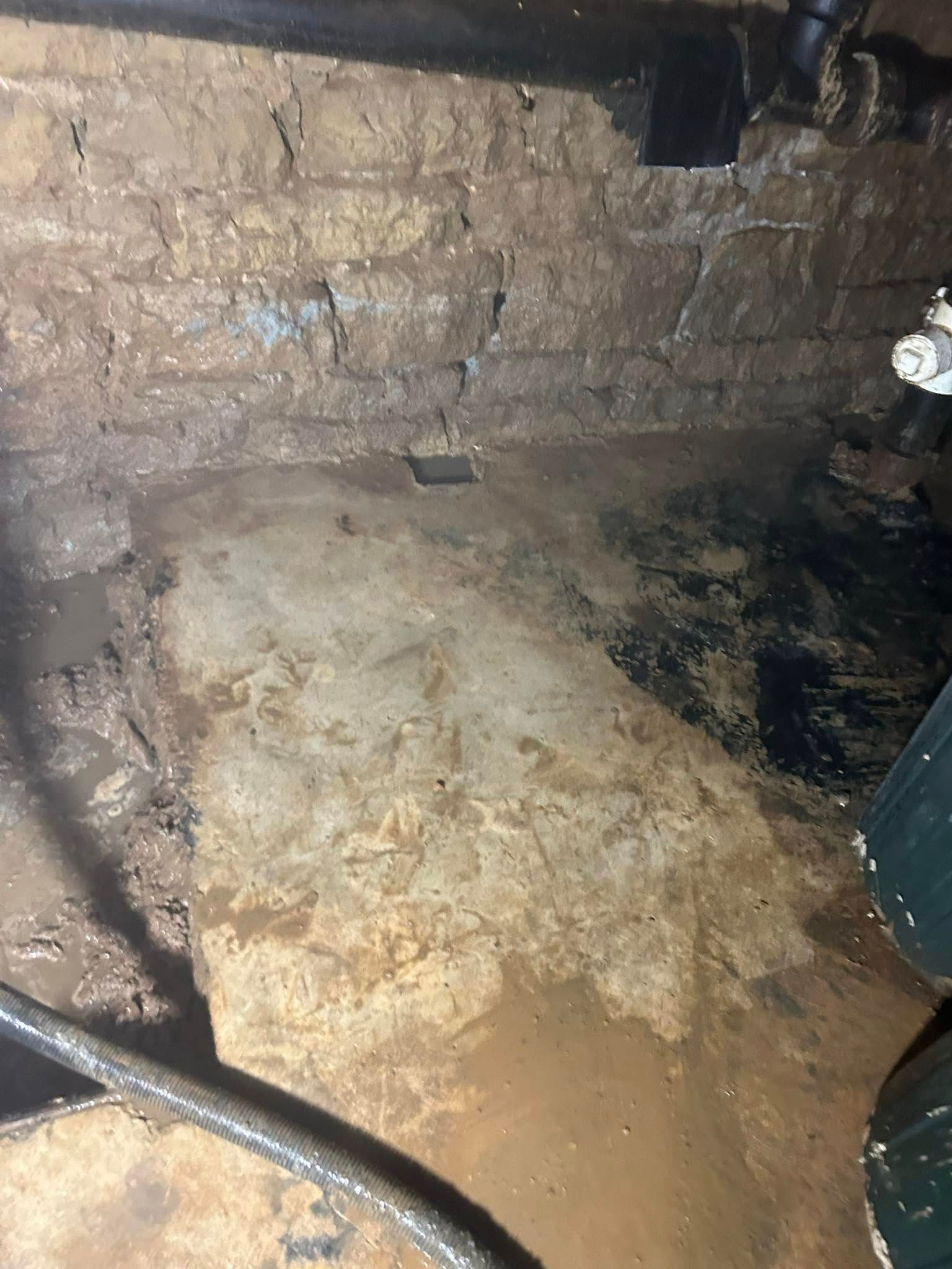 Wet, dirty basement with stone walls and standing water on the floor.