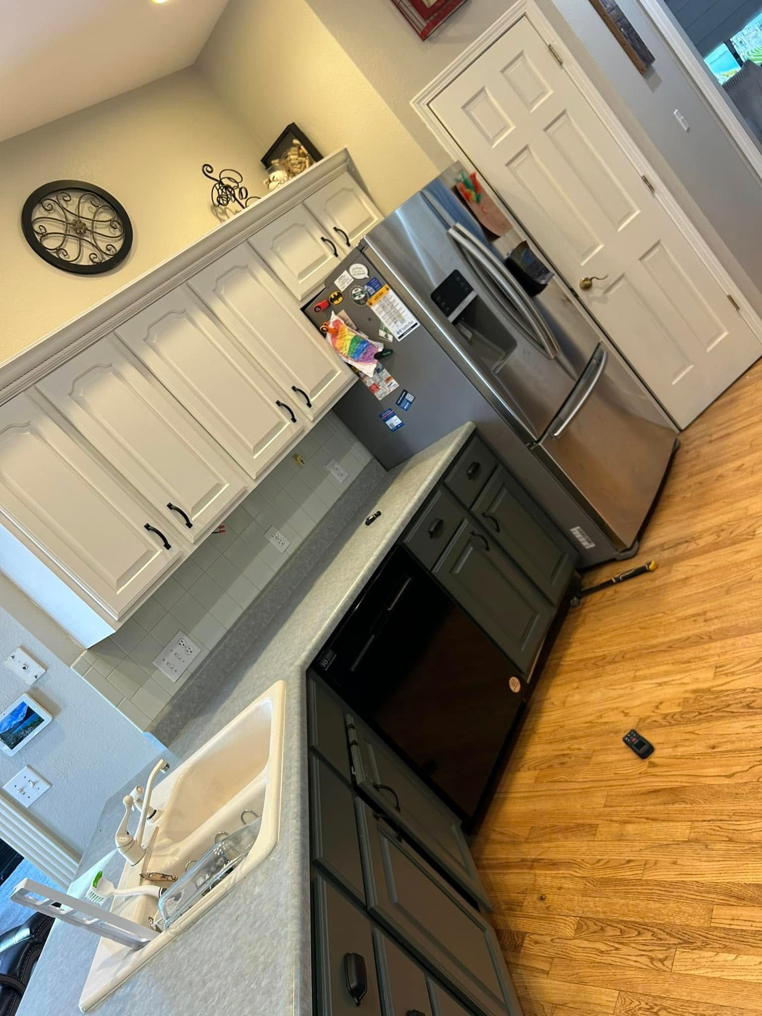 Kitchen with white upper cabinets, dark gray lower cabinets, stainless steel refrigerator, and wood floor.