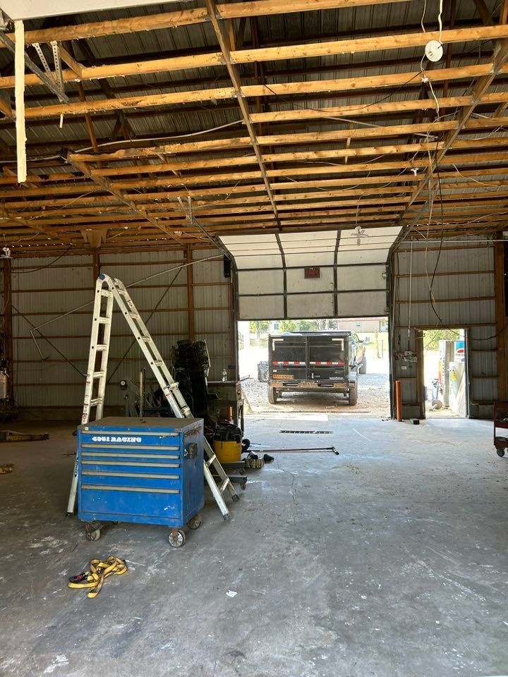 Interior of a large garage with an open door revealing a truck. A toolbox and ladder are in the foreground.