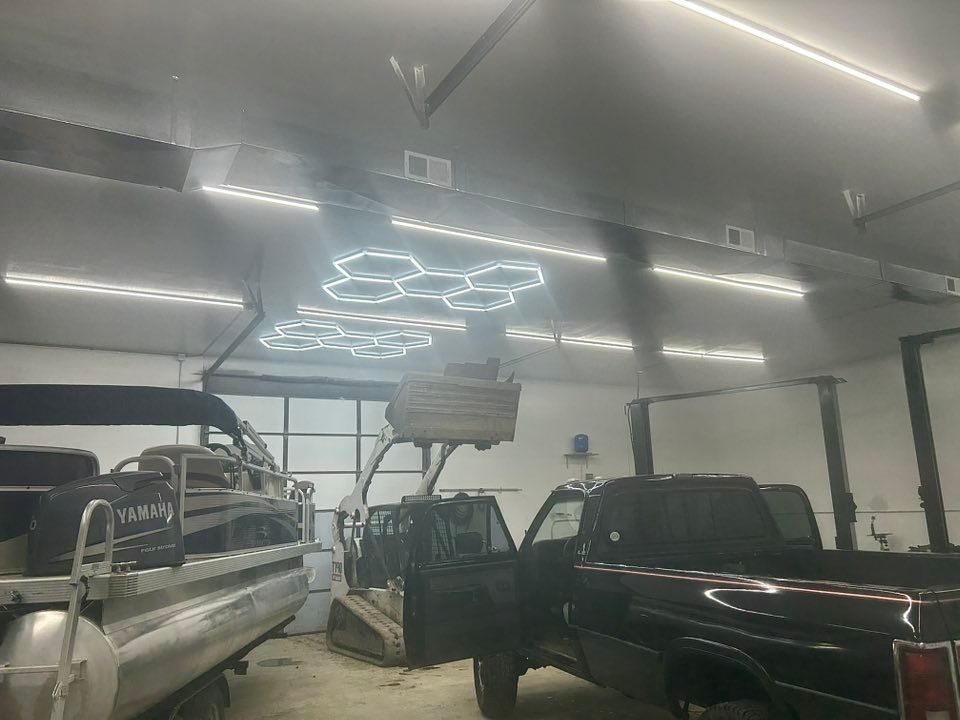 A workshop scene with a boat, trucks, and a lift machine under bright ceiling lights.