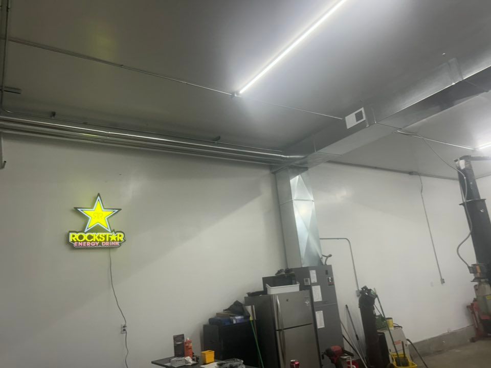A garage interior with a Rockstar energy drink sign, metal ductwork, and fluorescent lighting.