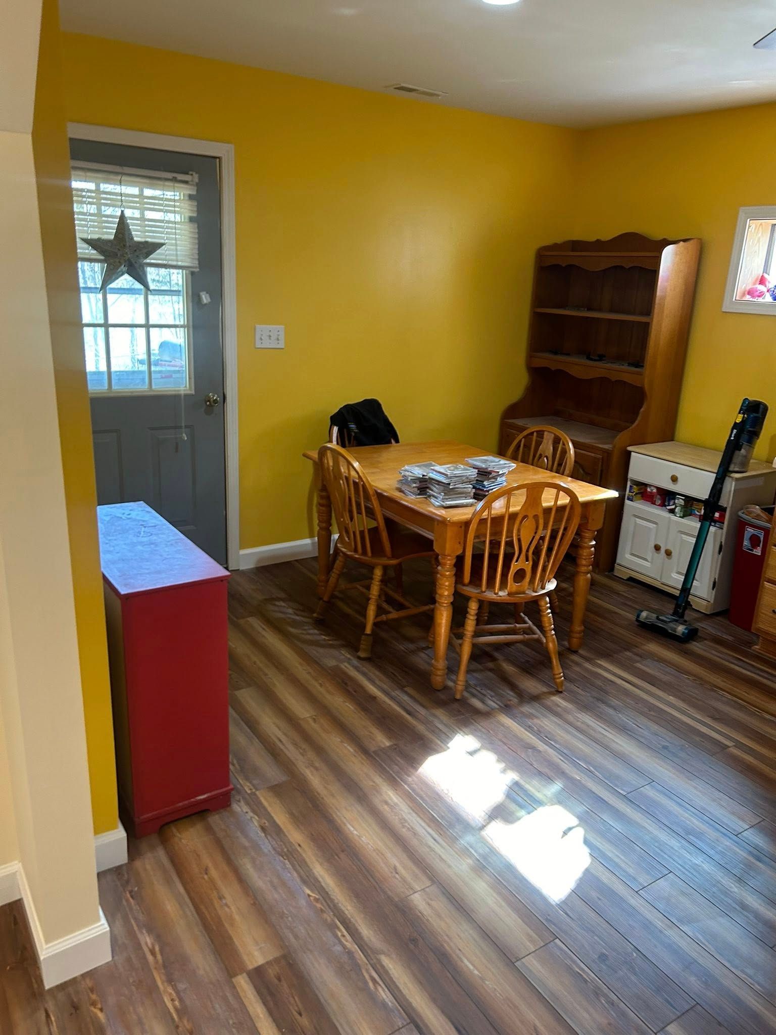 Dining room with wood table, chairs, hutch, red cabinet, yellow walls, and a door with a star.
