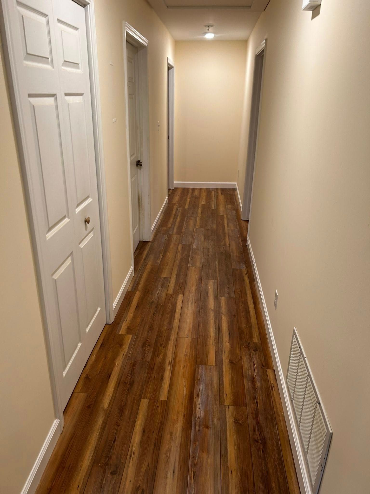 Hallway with wooden floor and beige walls, doors on both sides.