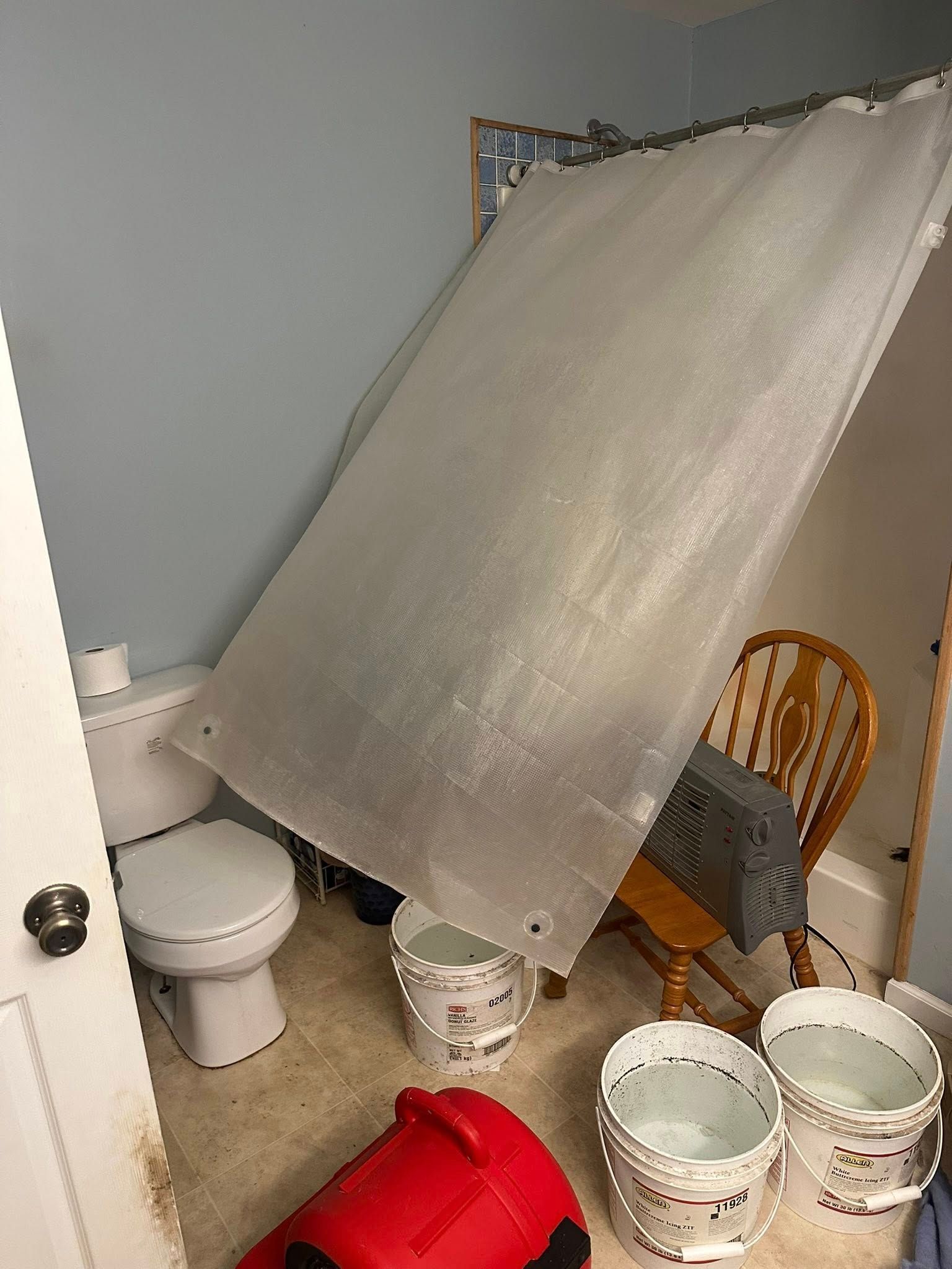 Bathroom with plastic sheeting, buckets, and a toilet. Possible water damage.