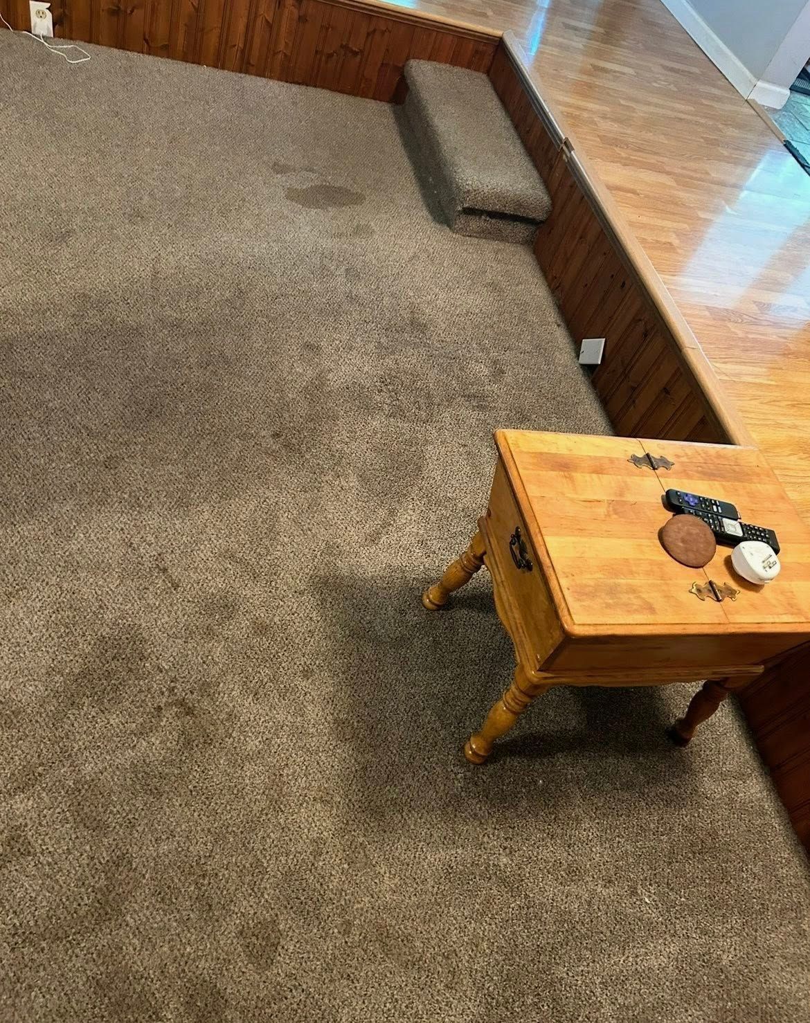 Brown carpeted room with wooden bench and small table.