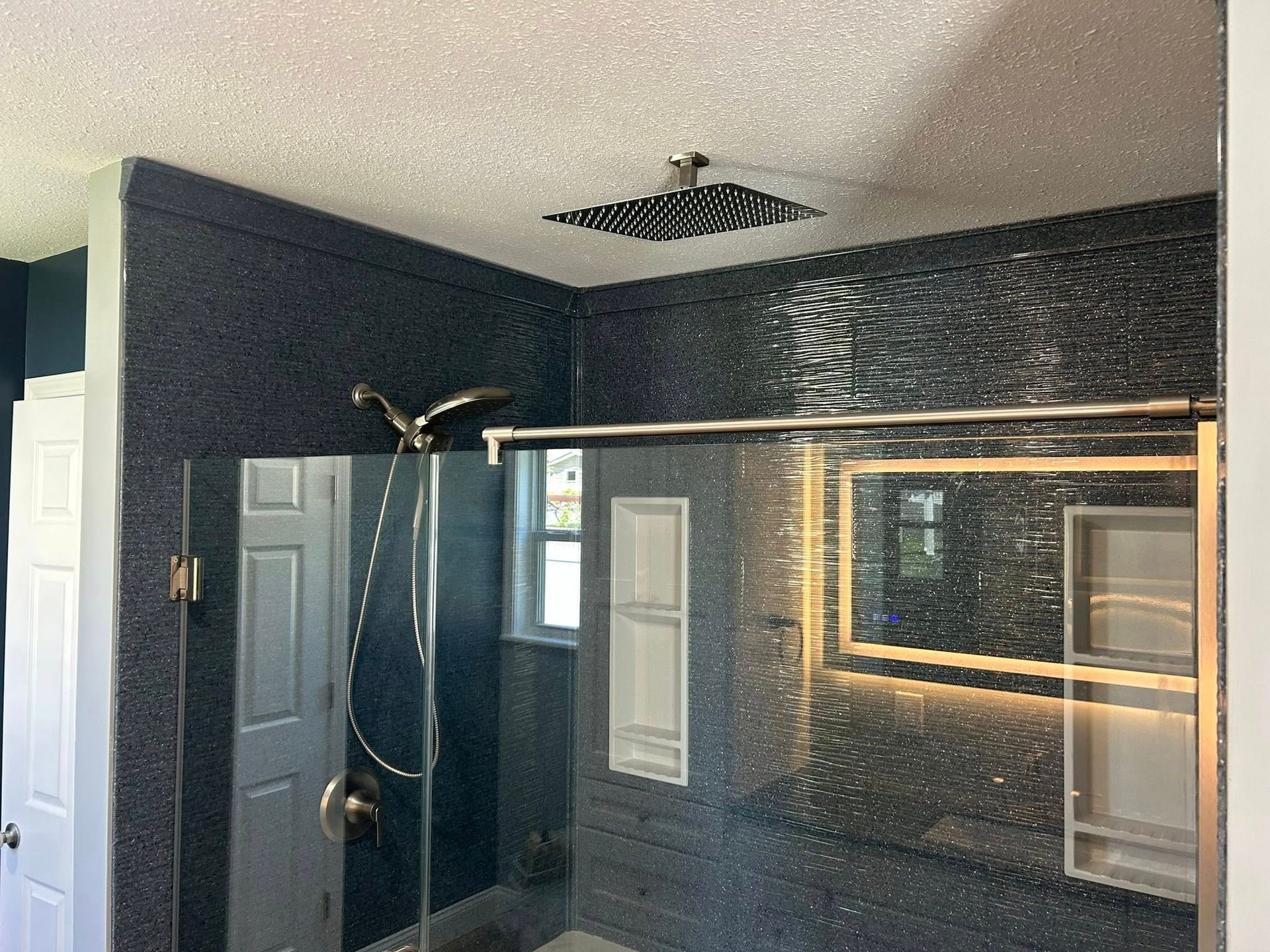 Modern bathroom with dark, textured tile, a rain showerhead, and glass shower enclosure.