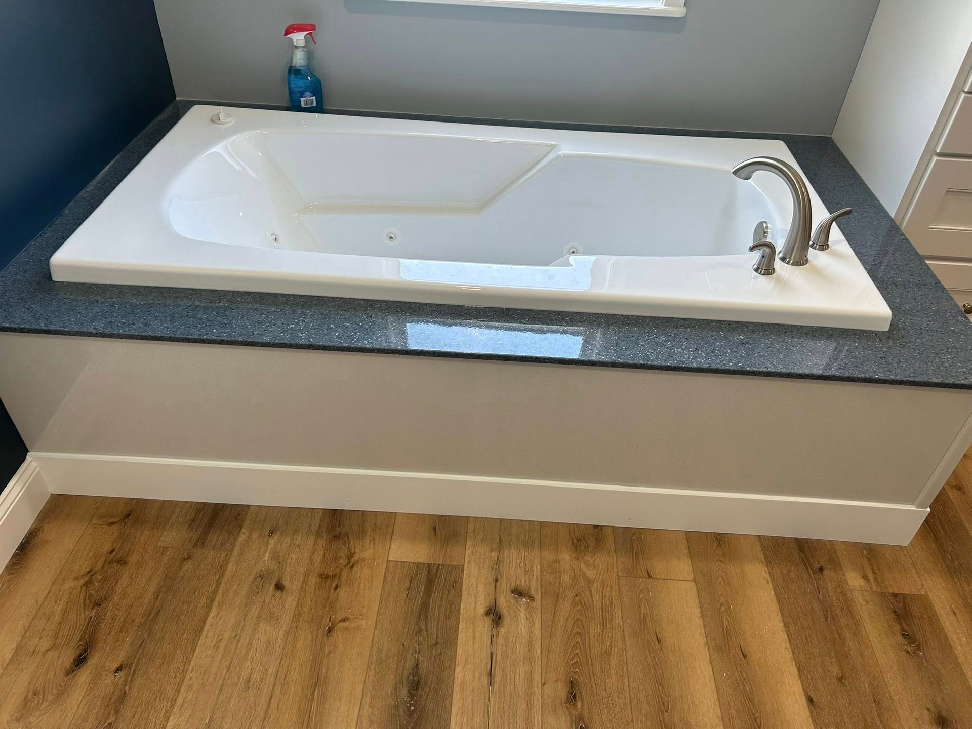 White bathtub on a gray countertop and white cabinet, bathroom interior with wood-look flooring.