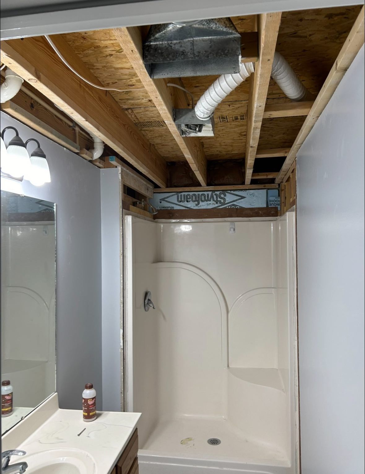 Bathroom under construction, with exposed ceiling beams and a white shower stall.