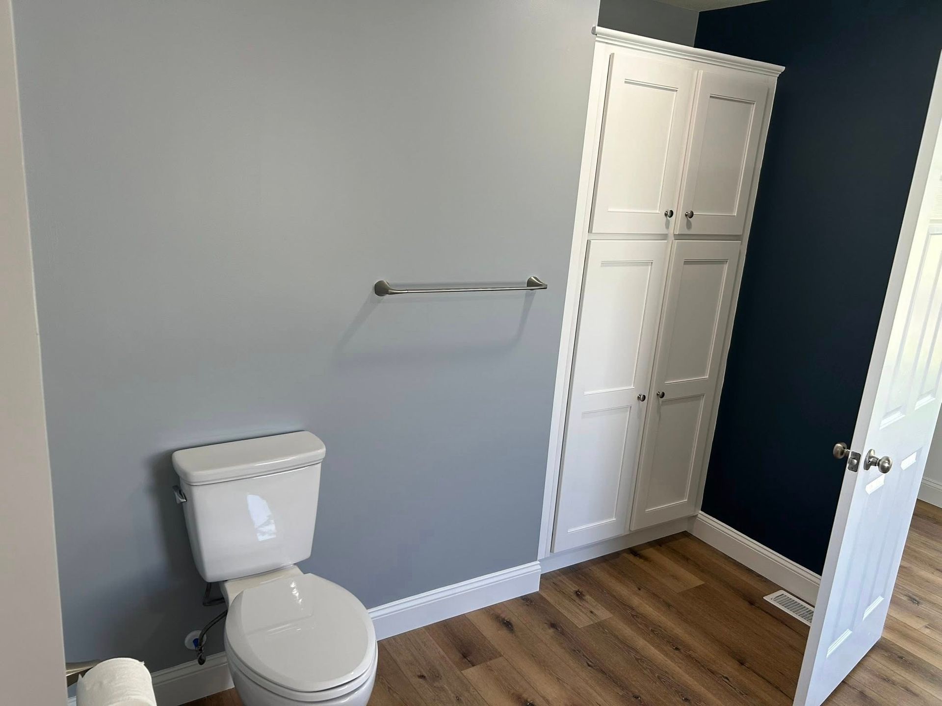 Bathroom with a white toilet, gray walls, tall white cabinet, and a towel rack.