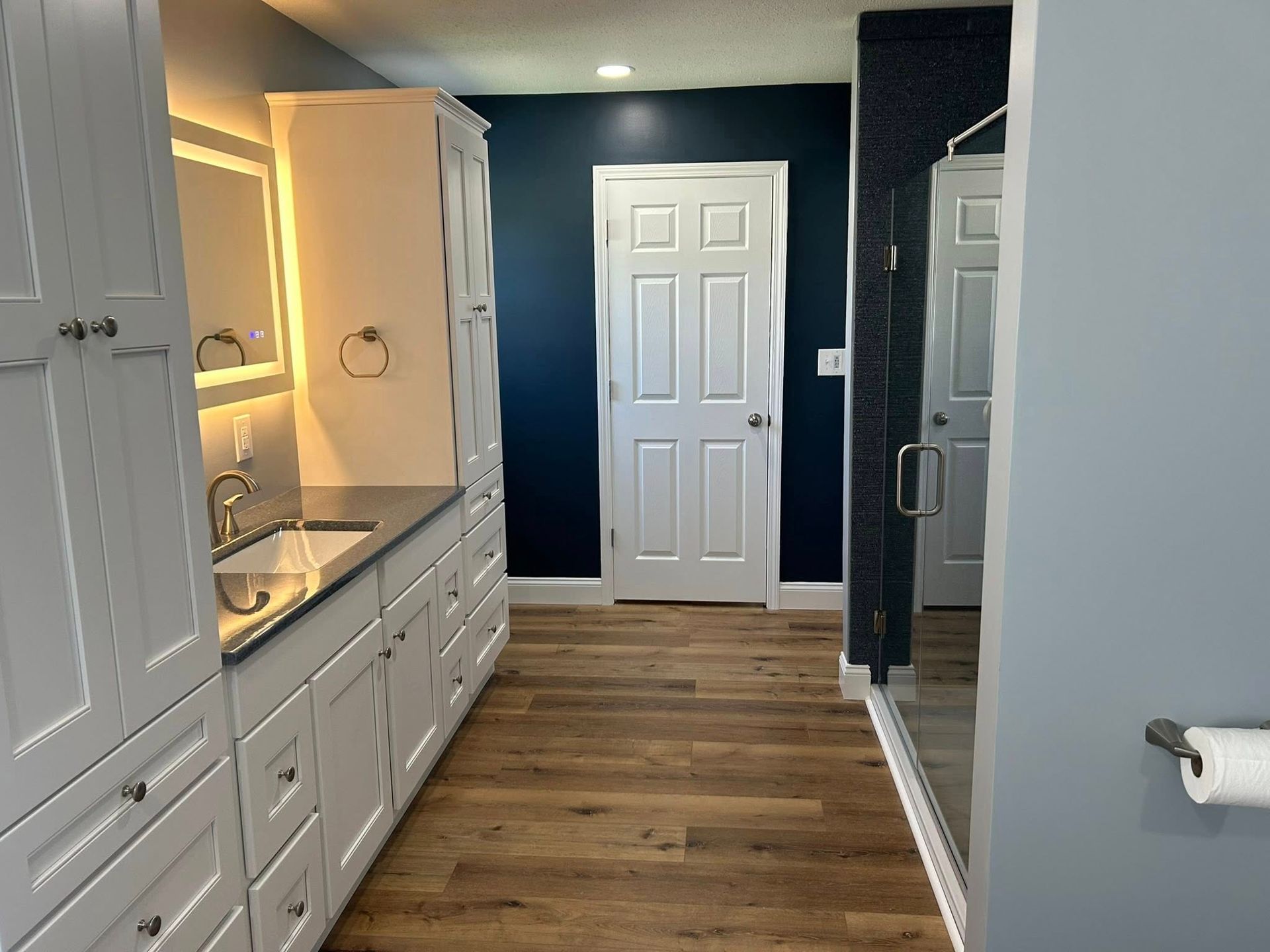 Bathroom with white cabinets, blue walls, a walk-in shower, and wood-look flooring.
