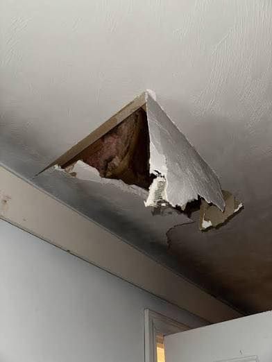 Hole in a white ceiling, exposing wood framing and insulation. Damaged drywall hangs down.