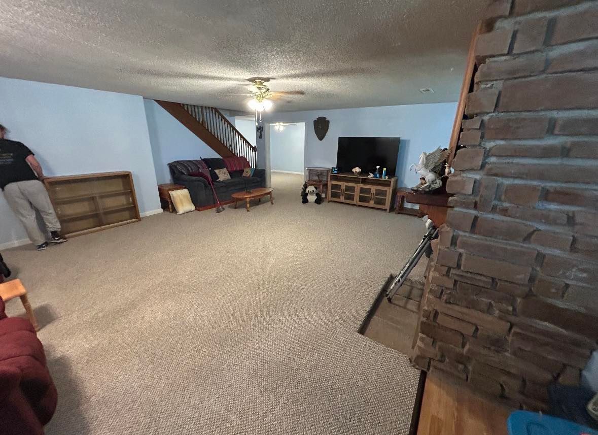 Spacious living room with blue walls, carpet, fireplace, sofa, staircase, and a person holding a bookshelf.