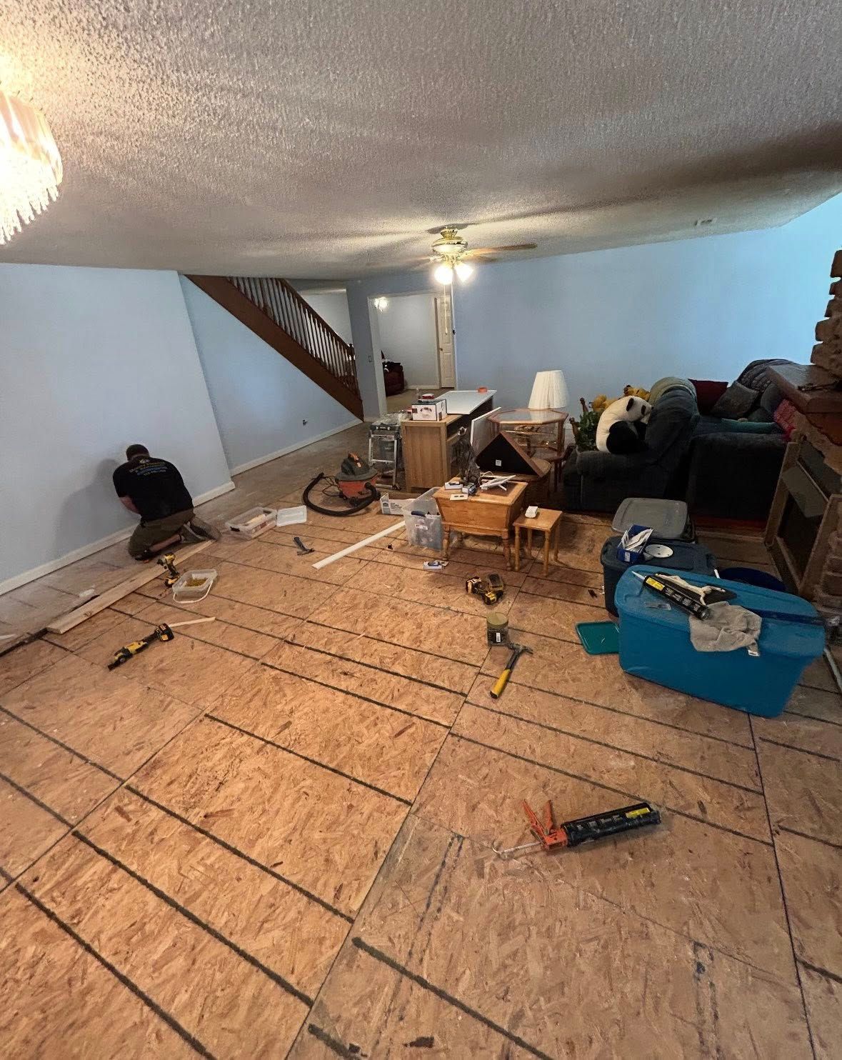 Room under renovation with exposed subfloor, tools, and a person working.