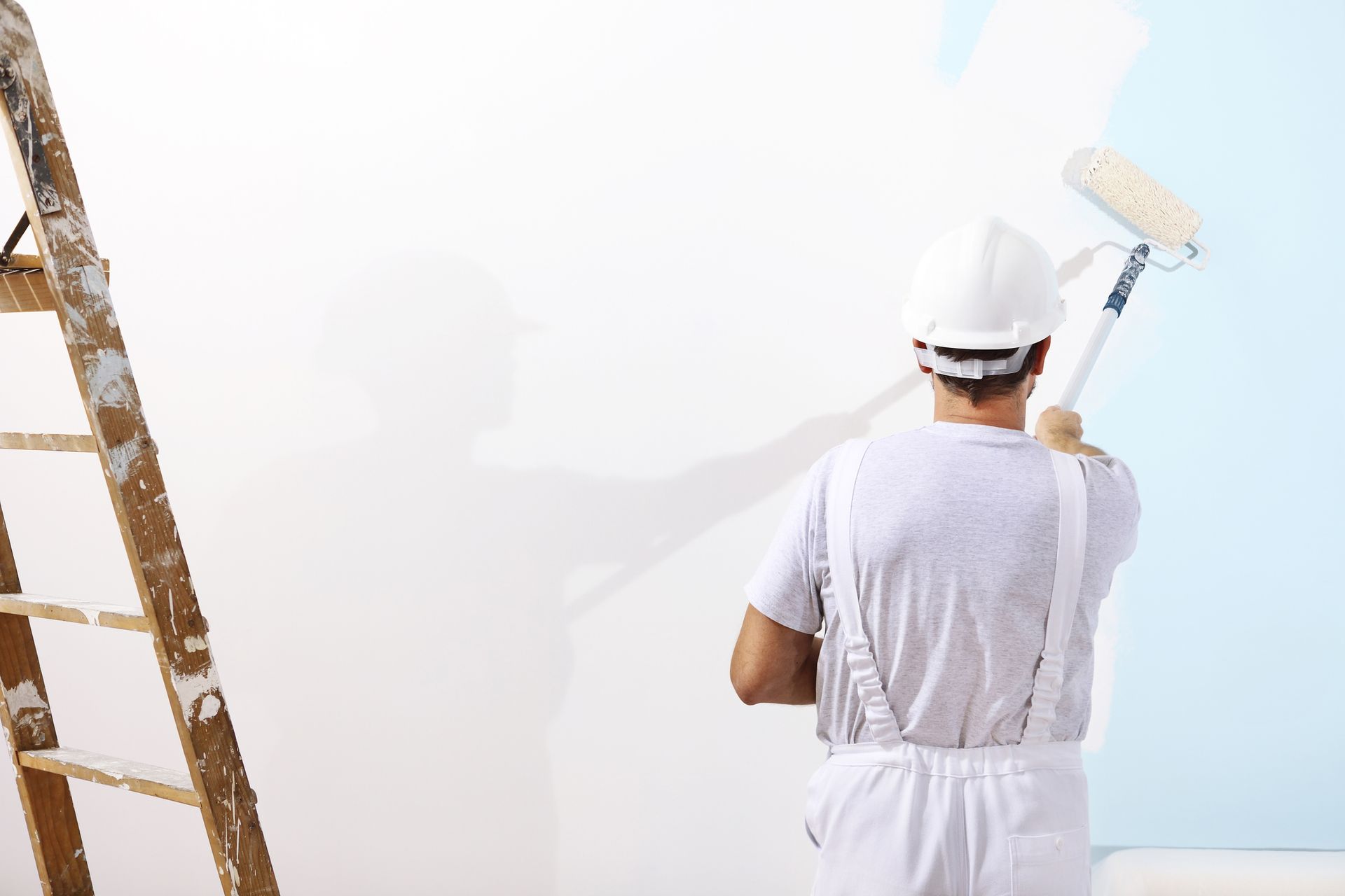 A man is painting a wall with a paint roller.