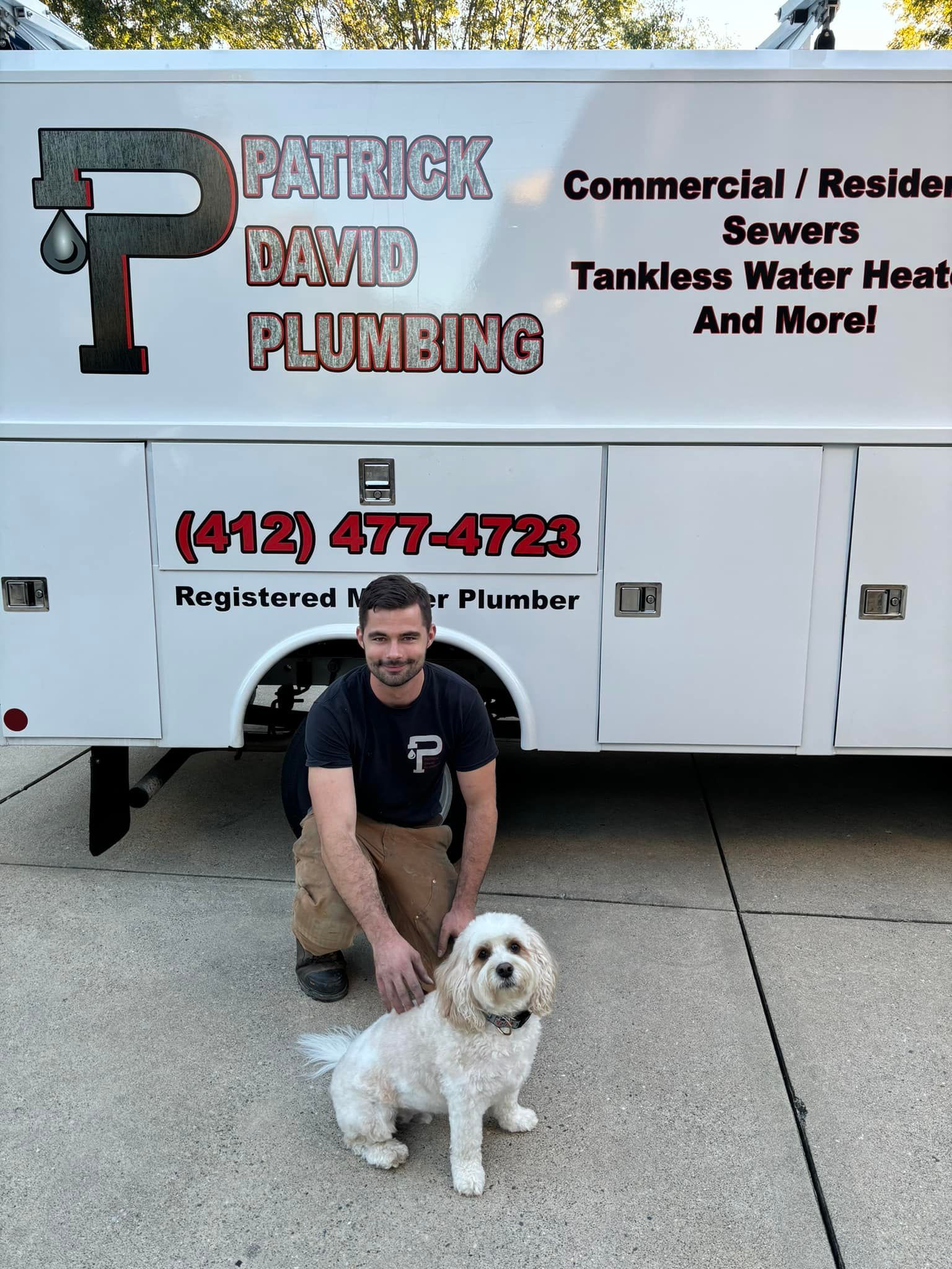 A man is kneeling next to a dog in front of a plumbing truck.