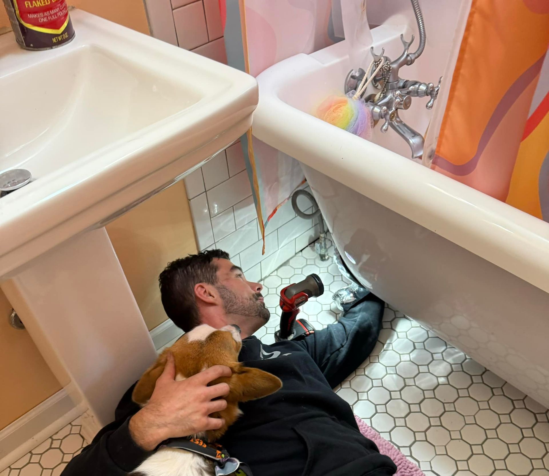 A man is fixing a bathtub in a bathroom with a dog
