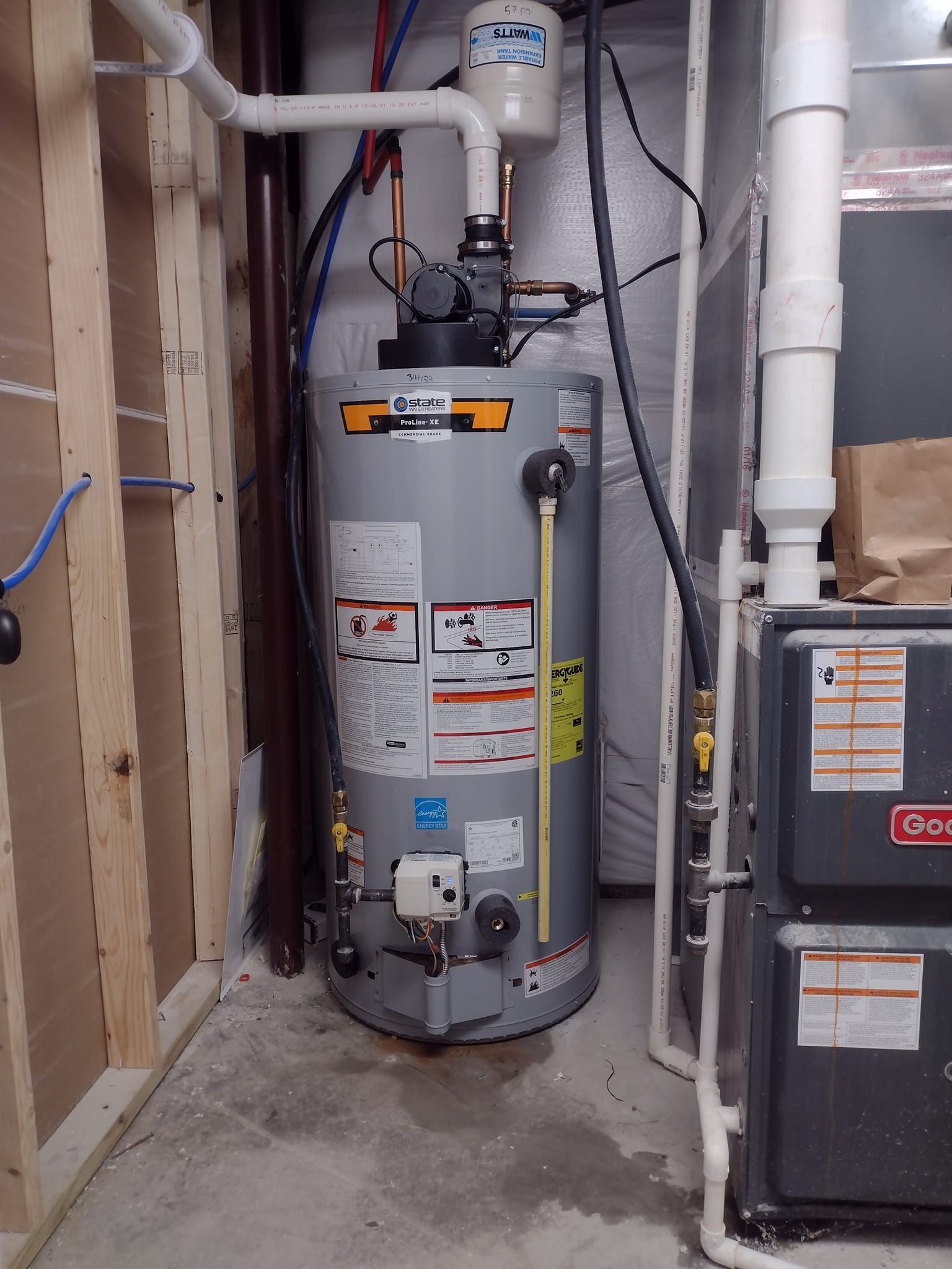 A water heater is sitting in a basement next to a furnace.