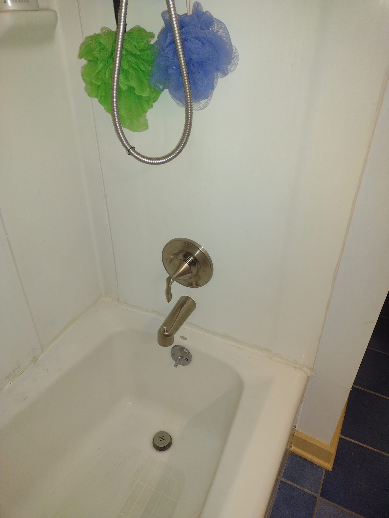 A bathtub with a shower head and sponges hanging from it