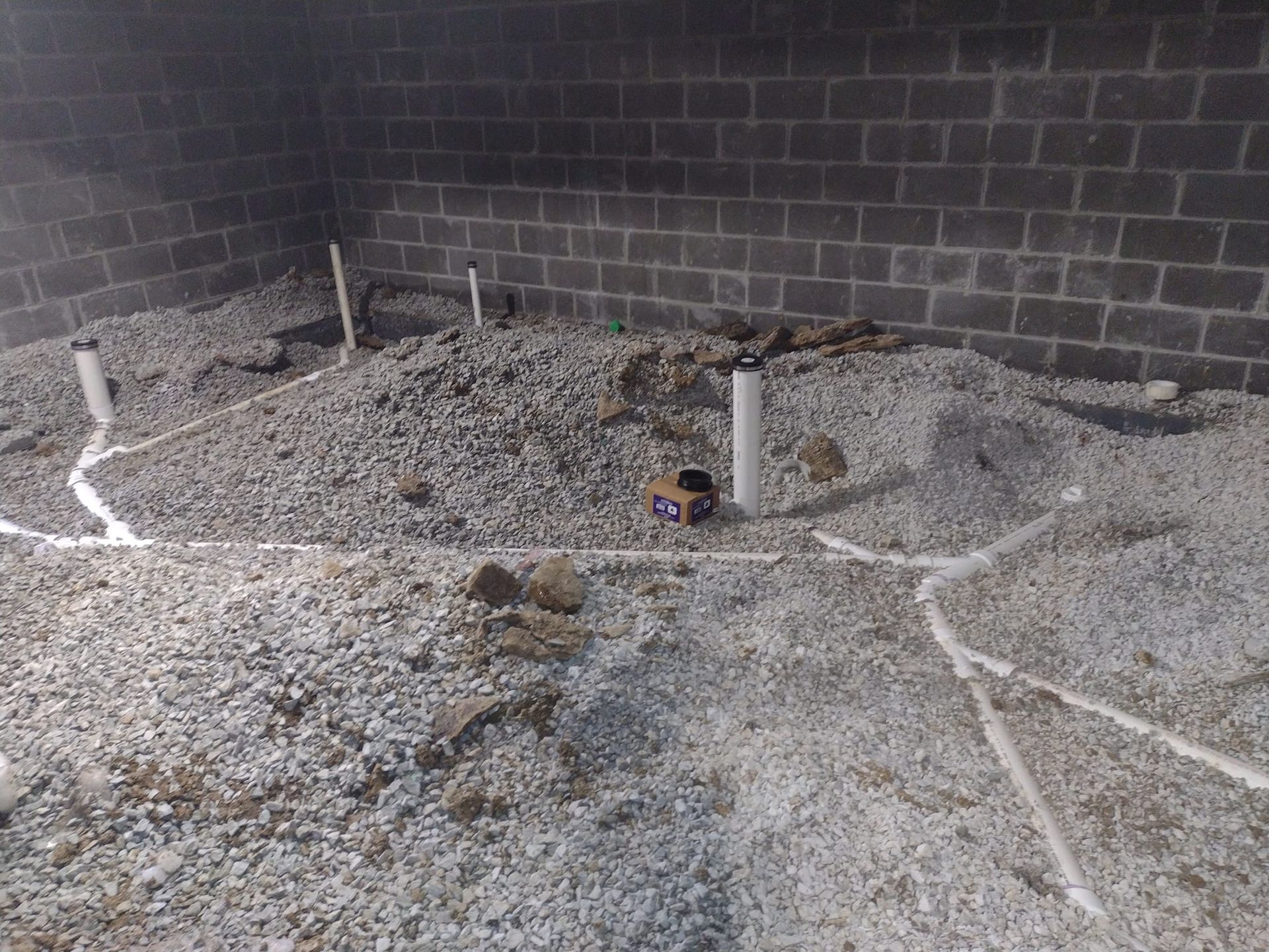 A room with gravel and pipes in it and a brick wall.