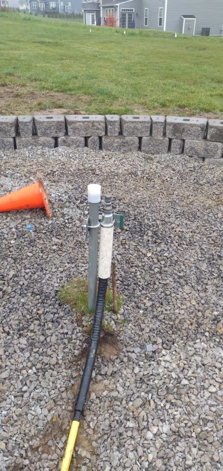 A hose is attached to a metal pole in a gravel area.