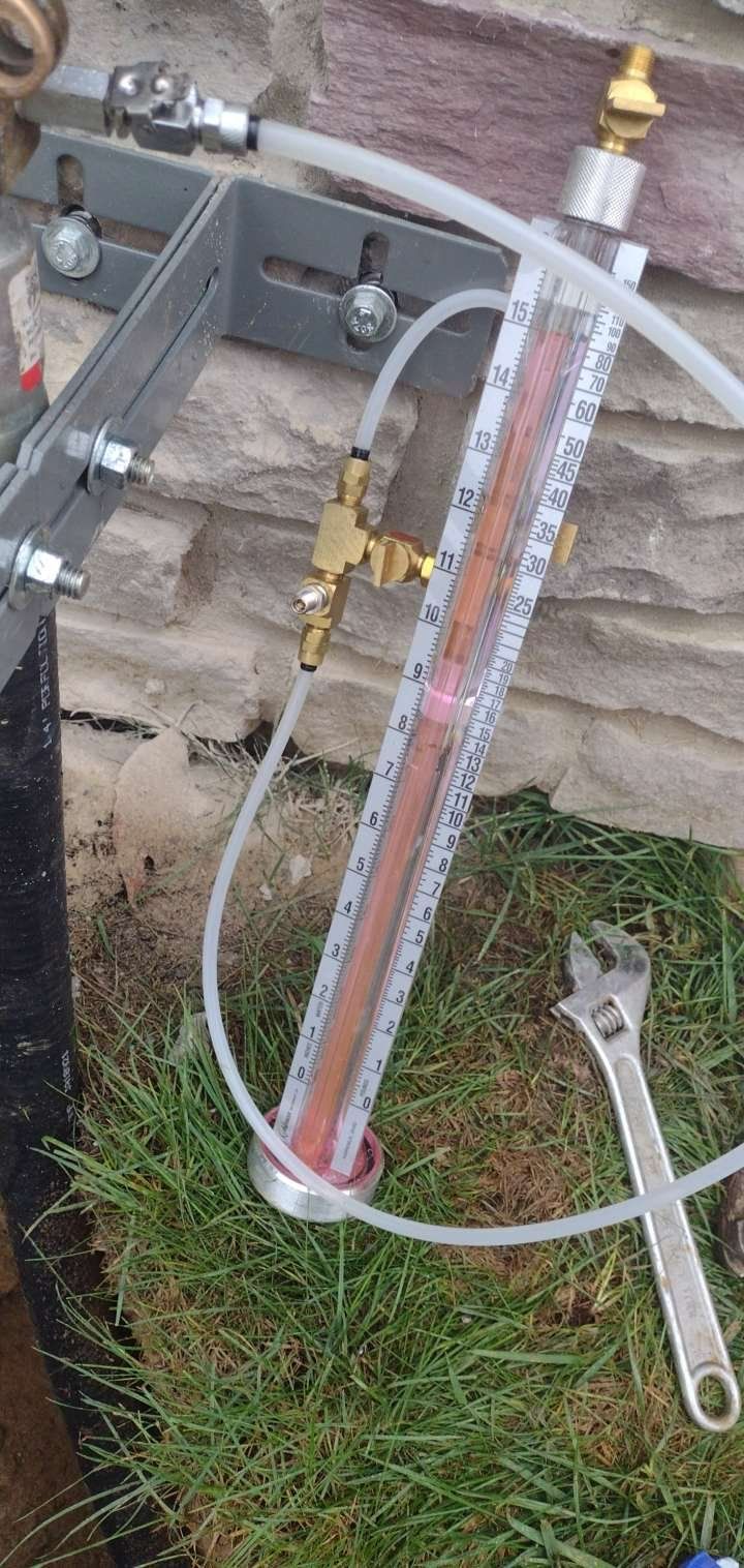 A pipe with a hose attached to it is sitting on the grass next to a wrench.