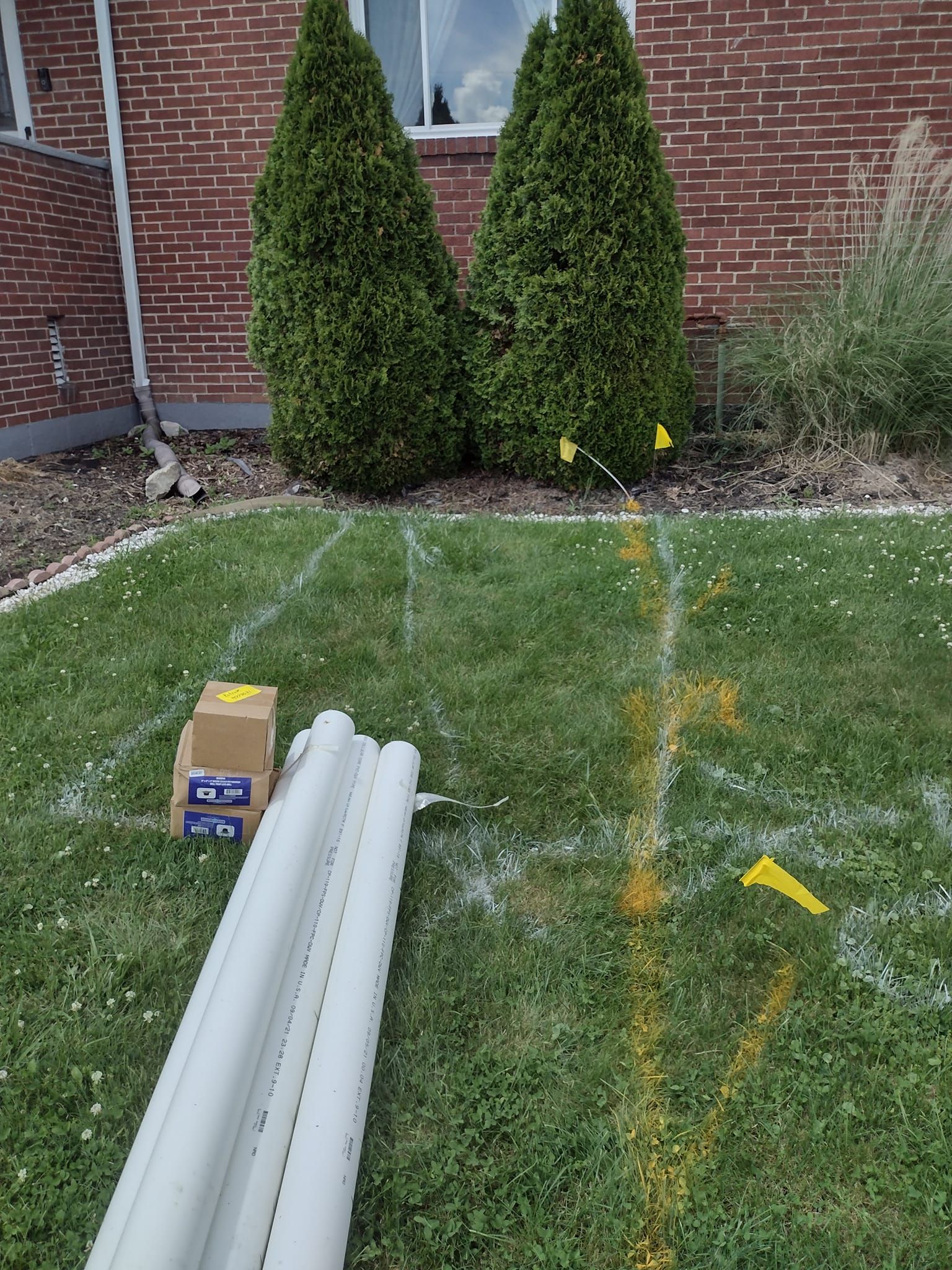 A bunch of pipes are laying on the grass in front of a house.