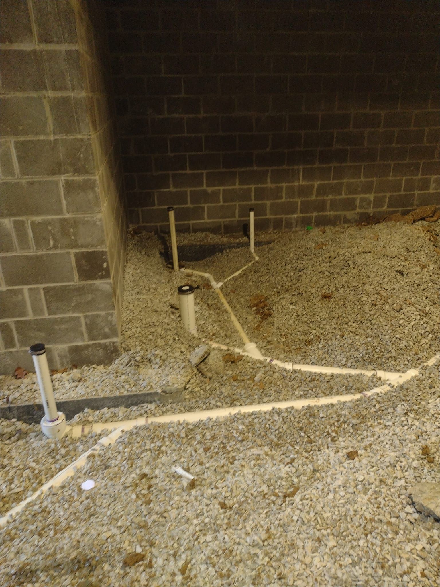A basement with a lot of pipes and gravel on the floor.