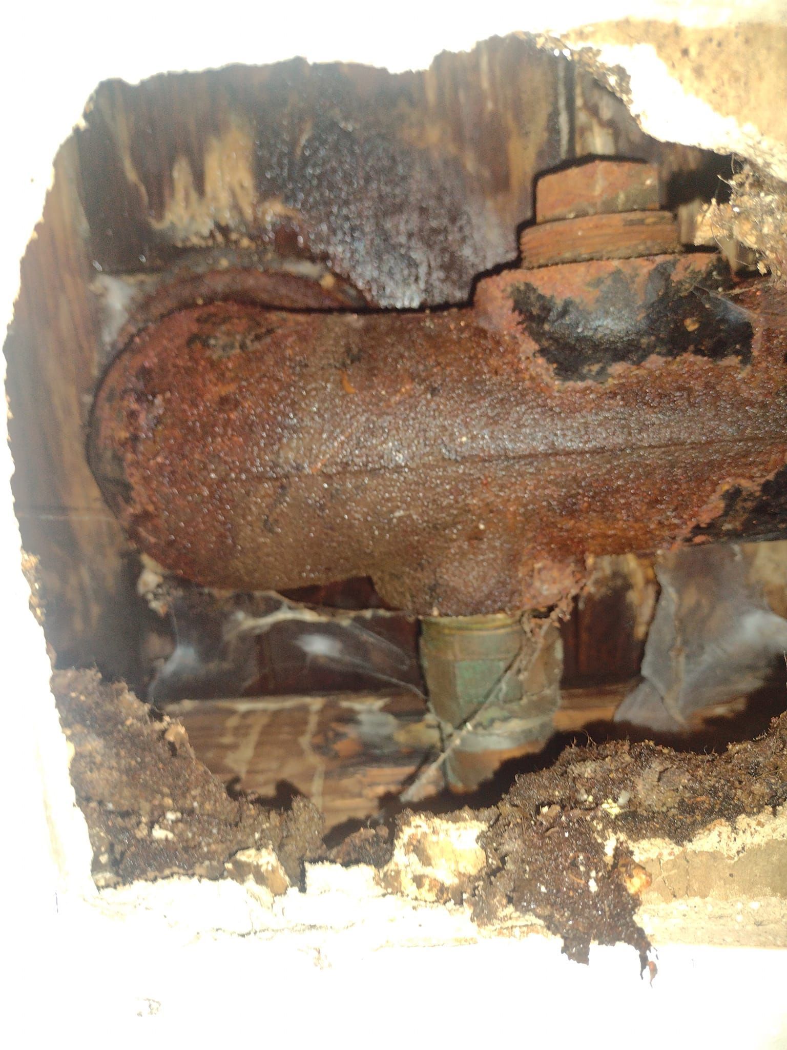 A close up of a rusty pipe in a hole in a wall.