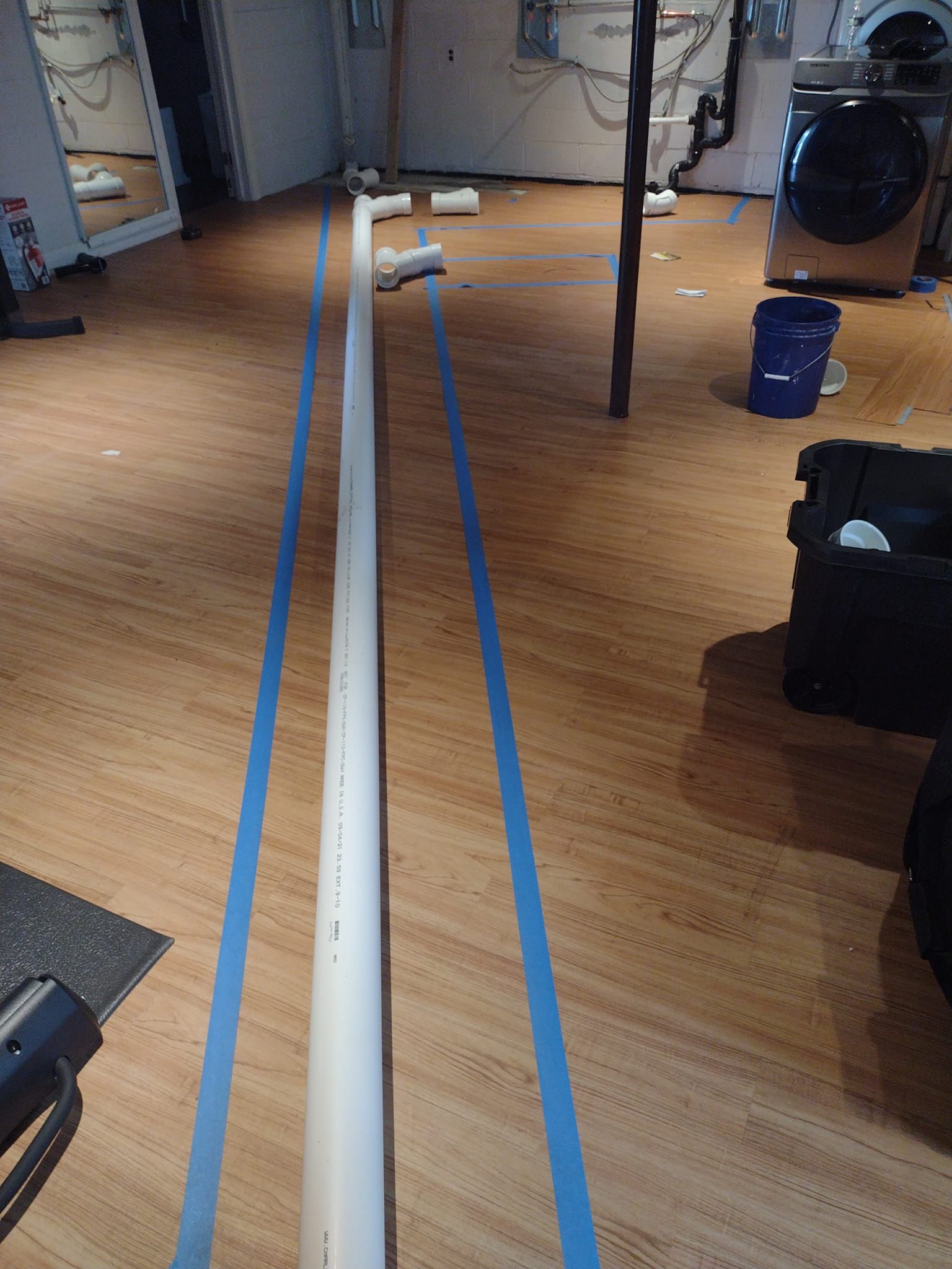 A long white pipe is taped to the floor in a basement