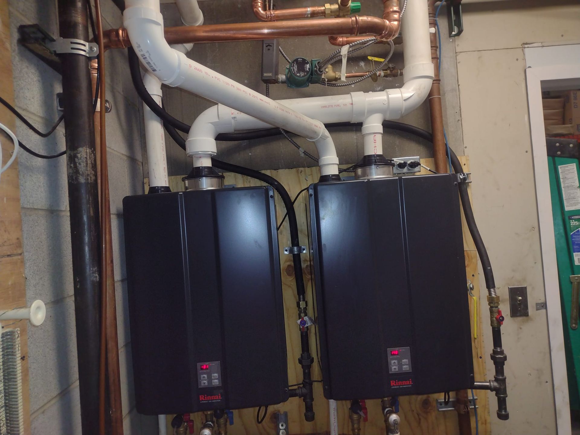 Two water heaters are connected to copper pipes in a basement.